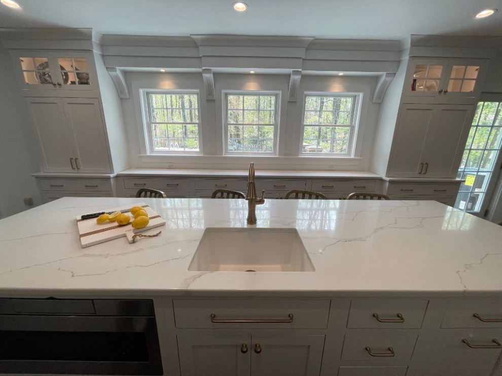 Farmhouse kitchen in Baltimore with a built-in sink, flat-panel cabinets, white cabinets, engineered stone countertops, engineered quartz splashback, stainless steel appliances, dark hardwood flooring and an island.