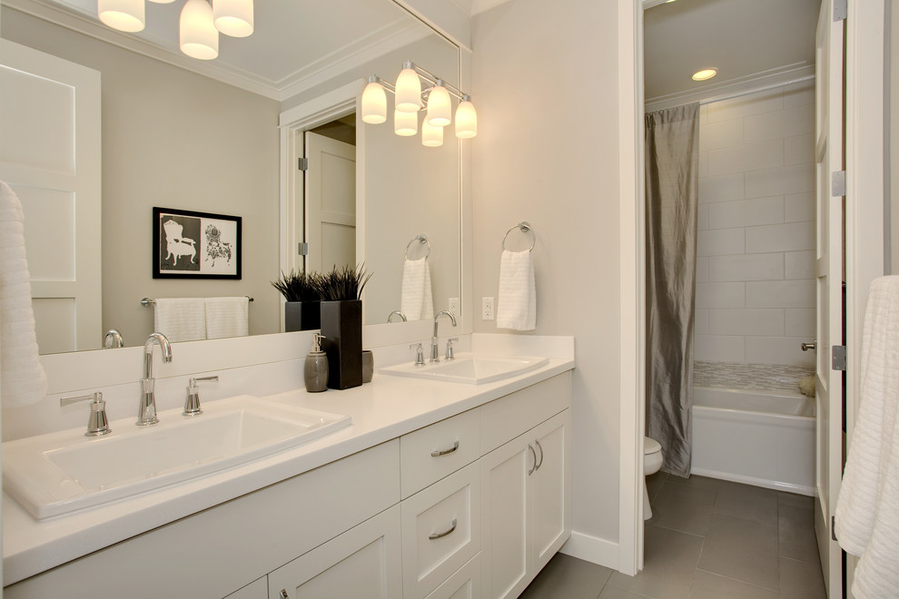 Photo of an arts and crafts kids bathroom in Seattle with a drop-in sink, recessed-panel cabinets, white cabinets, solid surface benchtops, an alcove tub, a shower/bathtub combo, white tile, porcelain tile, grey walls and porcelain floors.