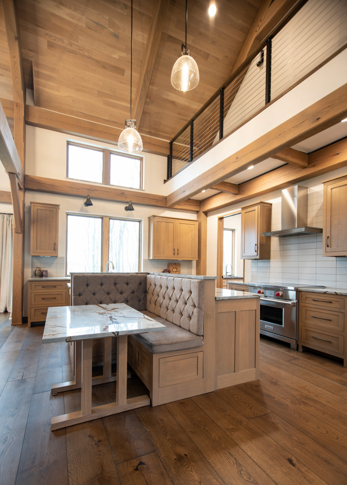 Example of a mountain style l-shaped medium tone wood floor and exposed beam kitchen design with shaker cabinets, light wood cabinets, quartzite countertops, gray backsplash, ceramic backsplash, stainless steel appliances and an island