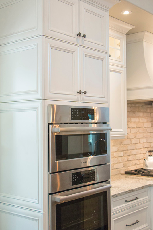 Example of a large transitional l-shaped home design design with a double-bowl sink, shaker cabinets, white cabinets, beige backsplash, stainless steel appliances and an island