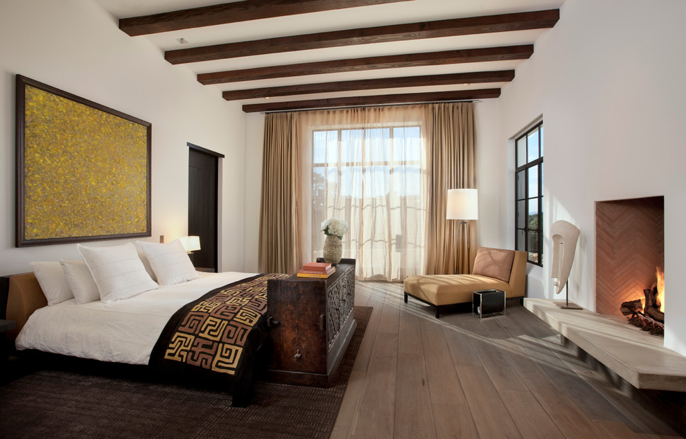 Mediterranean bedroom in Santa Barbara with white walls, dark hardwood floors and a standard fireplace.