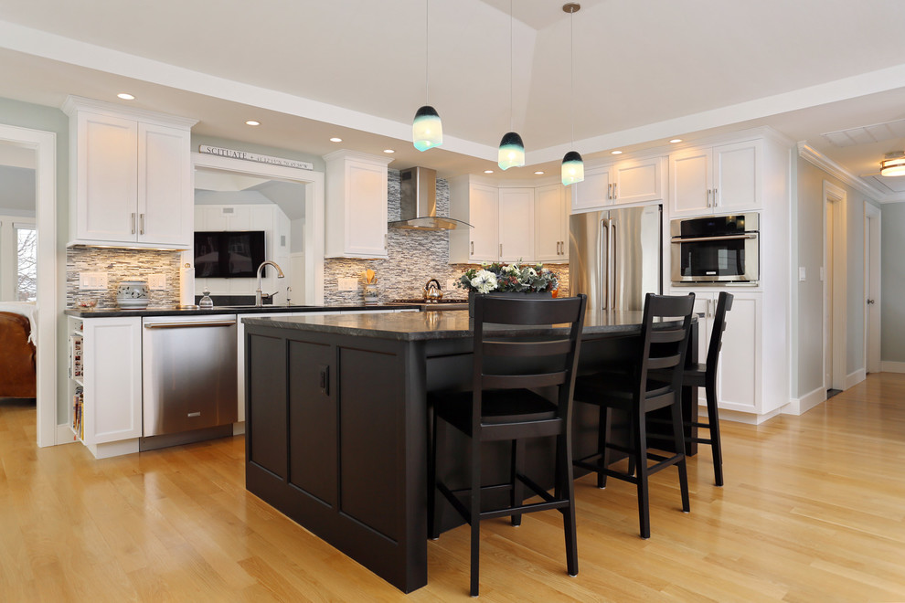 Inspiration for a mid-sized transitional l-shaped light wood floor open concept kitchen remodel in Boston with white cabinets, granite countertops, an island, an undermount sink, shaker cabinets, gray backsplash, matchstick tile backsplash and stainless steel appliances