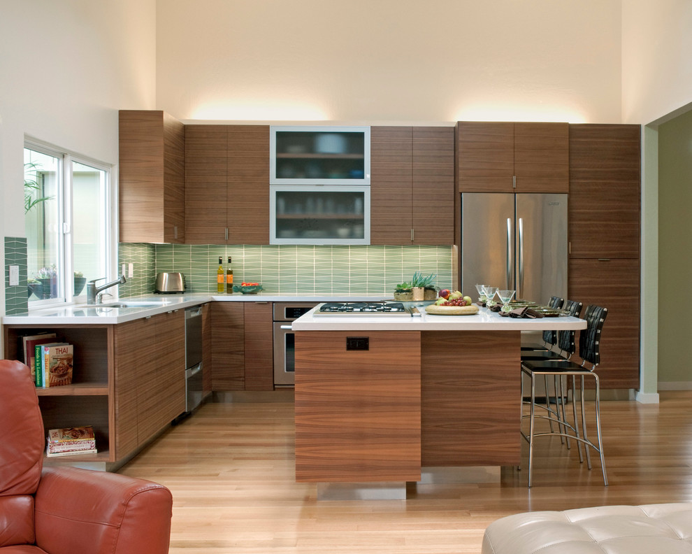 Design ideas for a midcentury l-shaped eat-in kitchen in San Francisco with an undermount sink, flat-panel cabinets, medium wood cabinets, solid surface benchtops, green splashback, stainless steel appliances, light hardwood floors, with island and glass tile splashback.