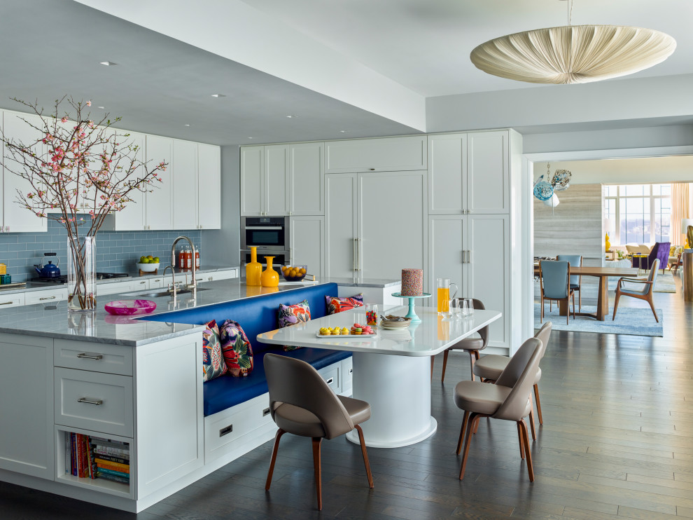 Photo of a transitional l-shaped eat-in kitchen in New York with an undermount sink, shaker cabinets, white cabinets, blue splashback, subway tile splashback, panelled appliances, dark hardwood floors, with island, brown floor and grey benchtop.