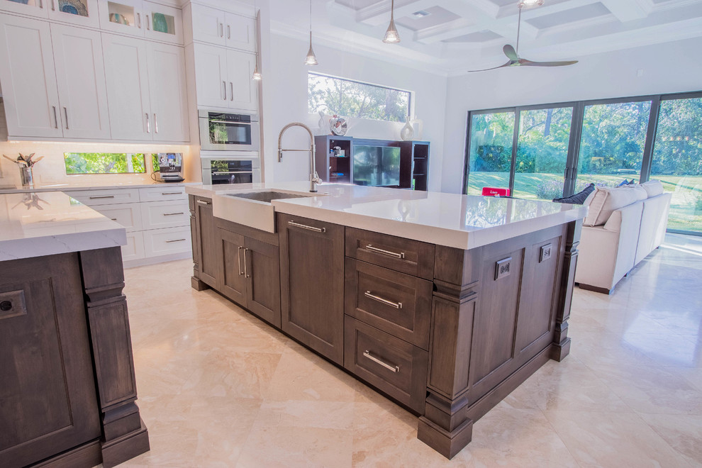Open concept kitchen - huge transitional l-shaped porcelain tile and beige floor open concept kitchen idea with a farmhouse sink, shaker cabinets, white cabinets, quartz countertops, white backsplash, porcelain backsplash, stainless steel appliances and two islands