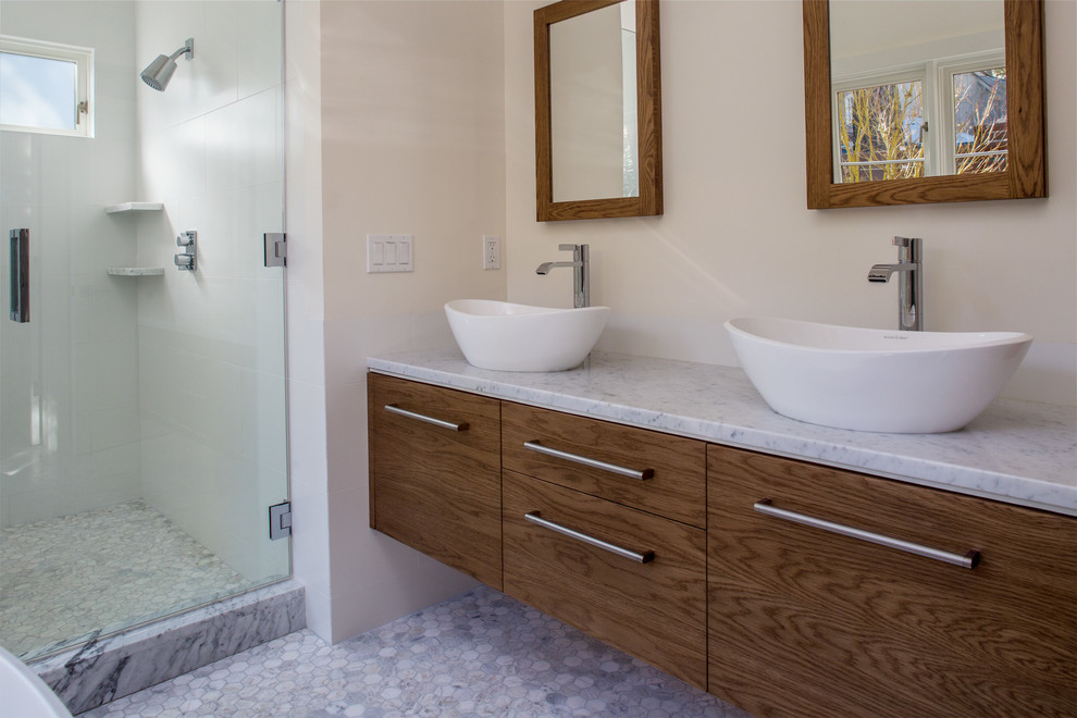 Photo of a modern bathroom in San Francisco with a vessel sink, flat-panel cabinets, medium wood cabinets, marble benchtops, a freestanding tub, an alcove shower, white tile, porcelain tile, white walls and marble floors.