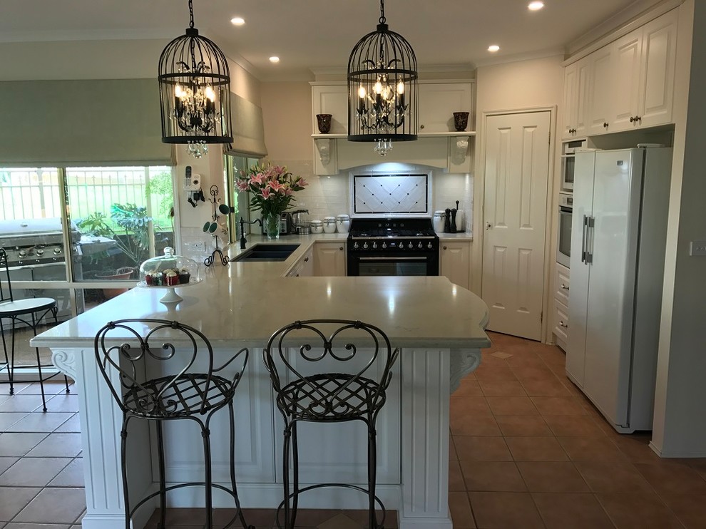 Inspiration for a mediterranean u-shaped eat-in kitchen in Melbourne with an undermount sink, subway tile splashback, black appliances, raised-panel cabinets, beige cabinets, granite benchtops, white splashback, terra-cotta floors and a peninsula.