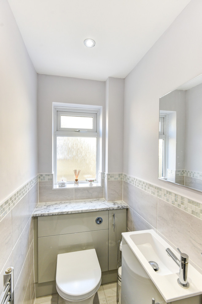Small modern grey and white family bathroom in Sussex with flat-panel cabinets, beige cabinets, a built-in bath, a shower/bath combination, grey tiles, ceramic tiles, grey walls, porcelain flooring, a built-in sink, laminate worktops, grey floors, a hinged door, grey worktops, a single sink and a built in vanity unit.