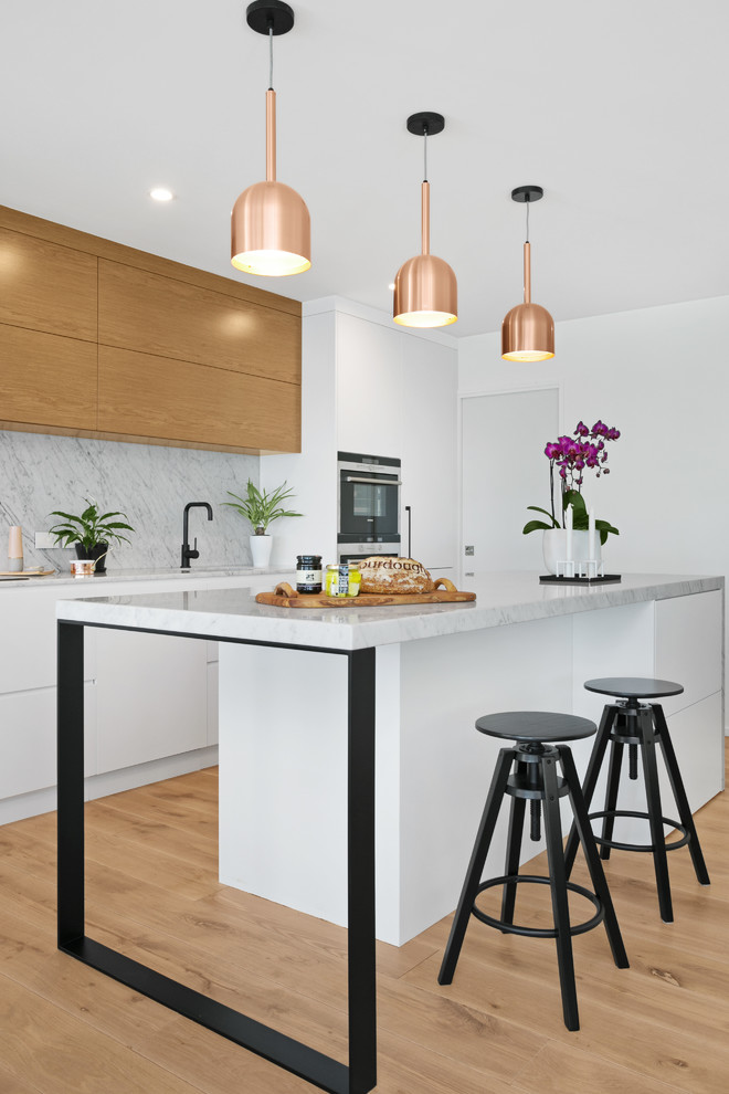 This is an example of a contemporary kitchen in Brisbane with flat-panel cabinets, stone slab splashback, with island, medium wood cabinets, grey splashback and light hardwood floors.