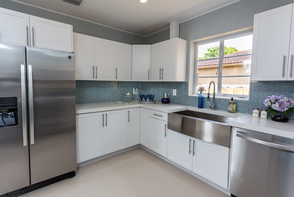 Photo of a mid-sized contemporary u-shaped eat-in kitchen in Miami with a farmhouse sink, shaker cabinets, white cabinets, granite benchtops, blue splashback, matchstick tile splashback, stainless steel appliances, linoleum floors, a peninsula and white floor.