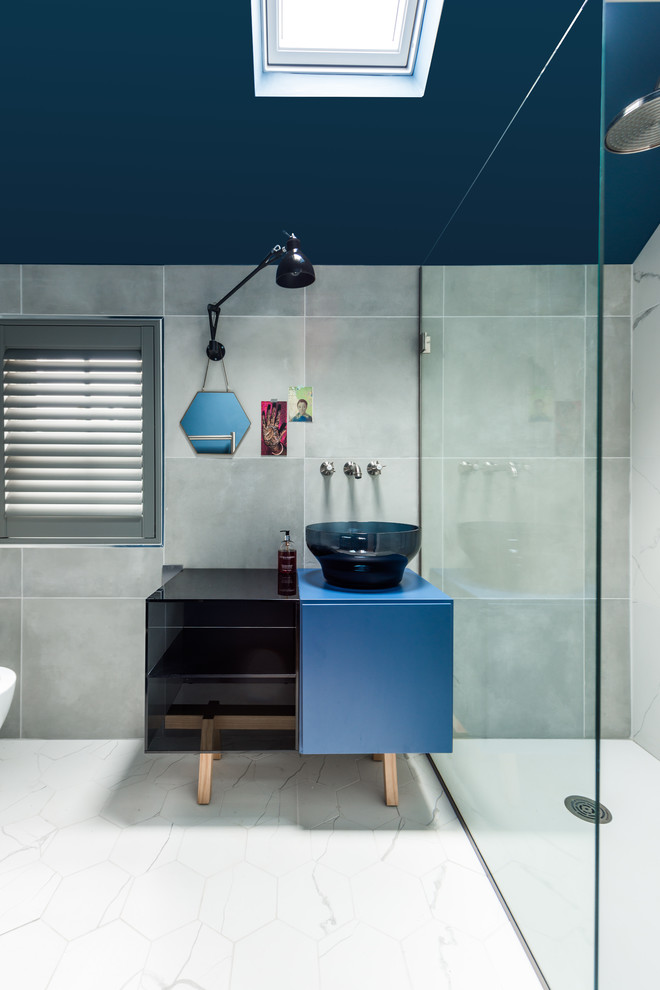 Mid-sized contemporary 3/4 bathroom in London with furniture-like cabinets, blue cabinets, an open shower, a one-piece toilet, gray tile, stone slab, grey walls, porcelain floors, a vessel sink and laminate benchtops.