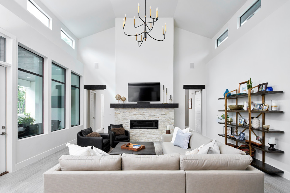 Transitional open concept living room in Austin with white walls, porcelain floors, a ribbon fireplace, a stone fireplace surround, a wall-mounted tv and grey floor.