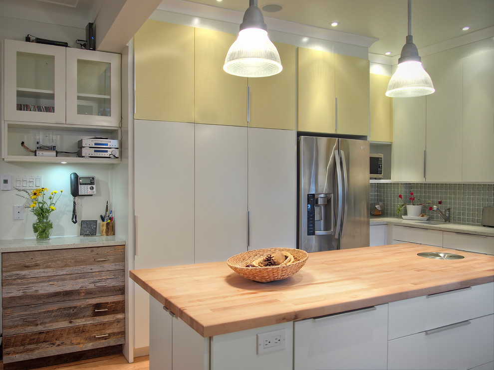 This is an example of a mid-sized transitional u-shaped eat-in kitchen in Montreal with an undermount sink, flat-panel cabinets, yellow cabinets, blue splashback, glass tile splashback, stainless steel appliances, light hardwood floors, with island and wood benchtops.