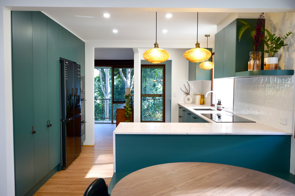Photo of a large transitional galley open plan kitchen in Sydney with an undermount sink, flat-panel cabinets, green cabinets, terrazzo benchtops, white splashback, subway tile splashback, black appliances, light hardwood floors, with island, brown floor and multi-coloured benchtop.