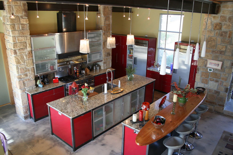 Large contemporary u-shaped open plan kitchen in Austin with a single-bowl sink, louvered cabinets, red cabinets, granite benchtops, beige splashback, stone slab splashback, stainless steel appliances, concrete floors and multiple islands.