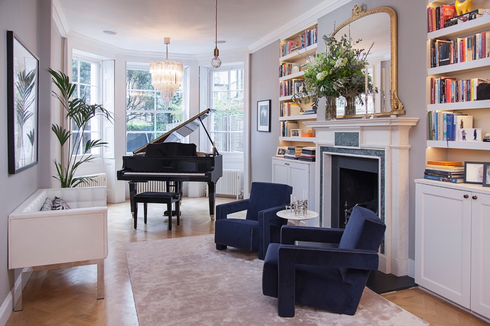 This is an example of a mid-sized transitional living room in London with a music area, grey walls, light hardwood floors, a standard fireplace, no tv and beige floor.