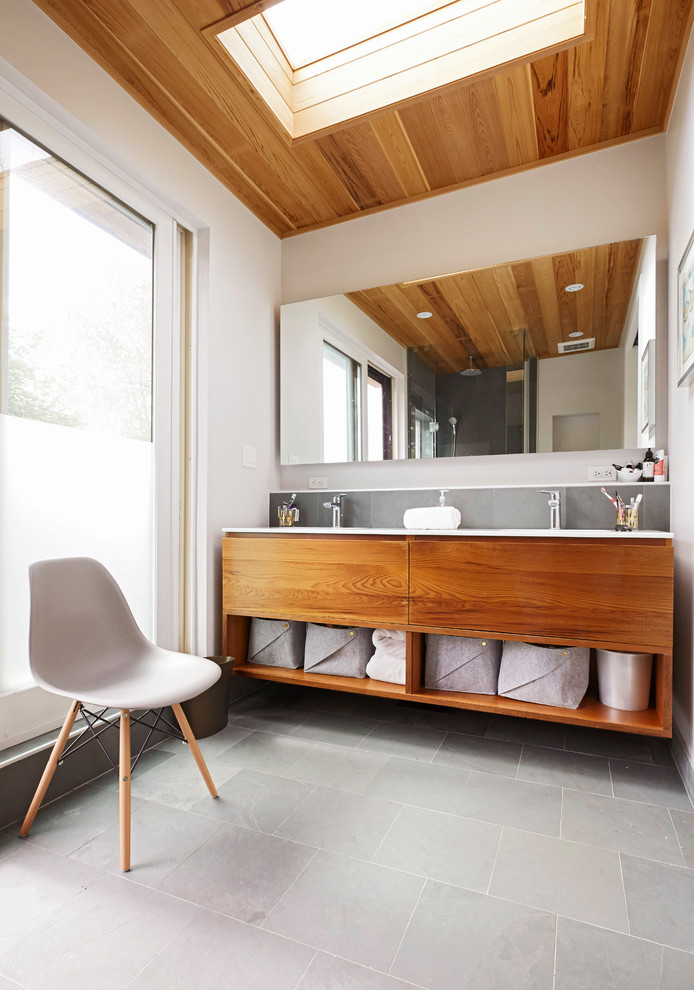 Photo of a mid-sized contemporary master bathroom in Toronto with flat-panel cabinets, medium wood cabinets, gray tile, white walls, grey floor, white benchtops, a corner shower, a two-piece toilet, slate, slate floors, an undermount sink, solid surface benchtops and a hinged shower door.