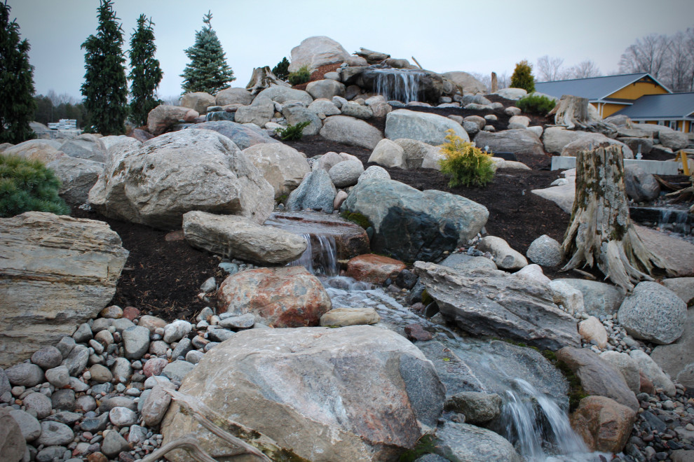 Inspiration for a huge rustic full sun hillside river rock waterfall.