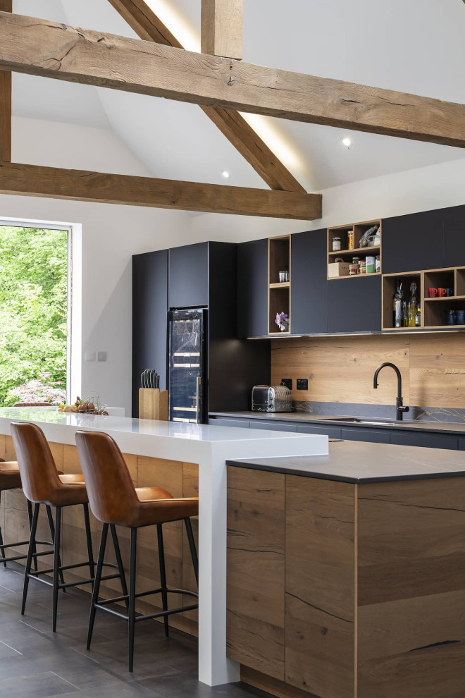 Photo of a mid-sized modern single-wall open plan kitchen in Oxfordshire with a double-bowl sink, flat-panel cabinets, black cabinets, quartzite benchtops, brown splashback, timber splashback, black appliances, with island, black floor, multi-coloured benchtop and exposed beam.