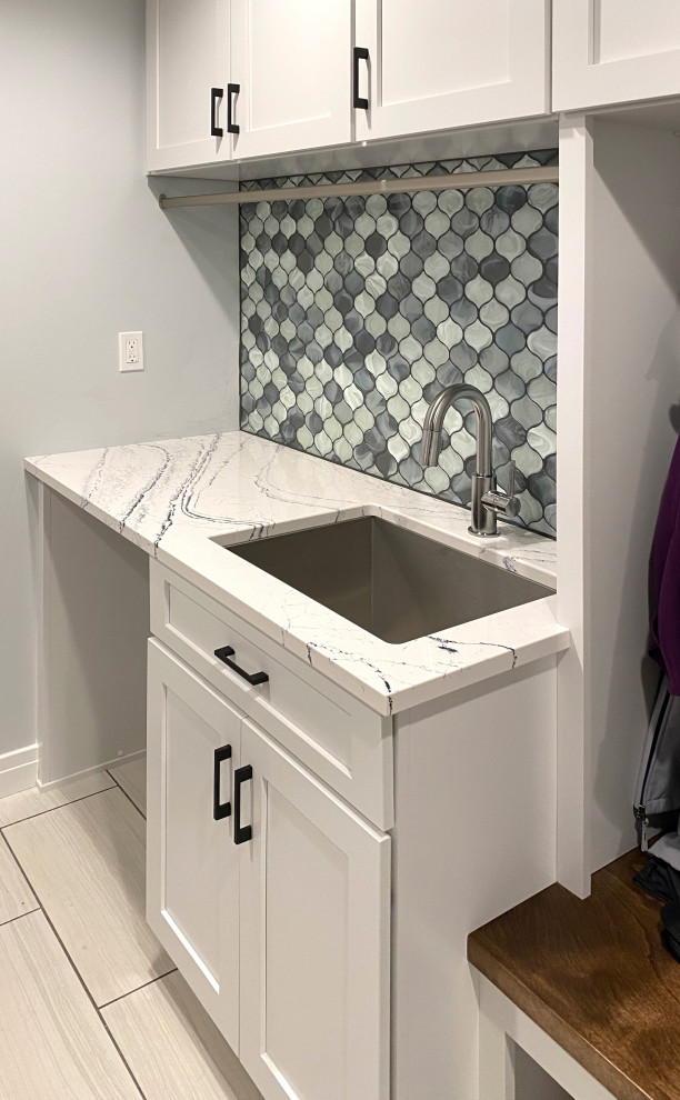 Inspiration for a mid-sized transitional galley dedicated laundry room in Other with an utility sink, shaker cabinets, white cabinets, quartz benchtops, blue splashback, glass tile splashback, white walls, ceramic floors, beige floor and multi-coloured benchtop.