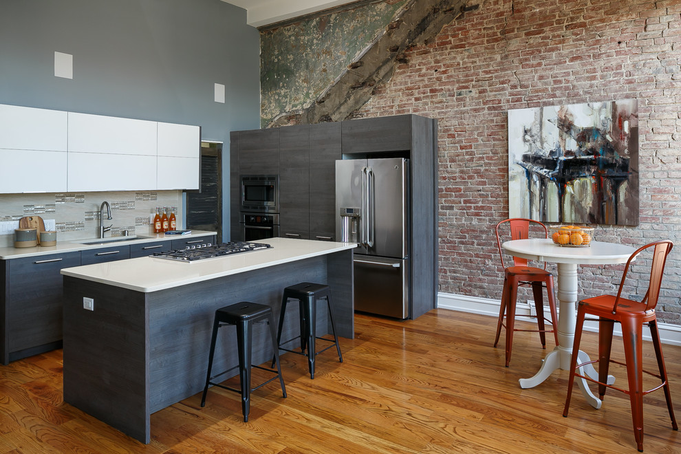 This is an example of an industrial eat-in kitchen in Louisville with an undermount sink, flat-panel cabinets, stainless steel appliances, medium hardwood floors, with island, white benchtop, white cabinets and multi-coloured splashback.