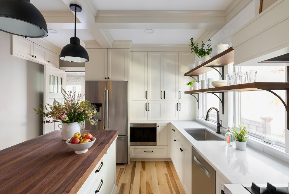 Inredning av ett klassiskt avskilt, mellanstort vit vitt u-kök, med en undermonterad diskho, luckor med infälld panel, vita skåp, bänkskiva i kvarts, vitt stänkskydd, stänkskydd i keramik, rostfria vitvaror, ljust trägolv, en köksö och brunt golv