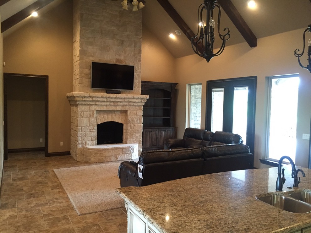 Photo of a mid-sized country open concept living room in Oklahoma City with a standard fireplace, a stone fireplace surround, a wall-mounted tv, beige walls and travertine floors.