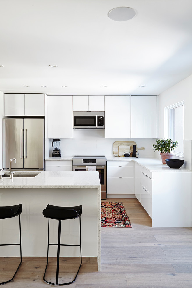 Photo of a scandinavian kitchen in Toronto with an undermount sink, flat-panel cabinets, white cabinets, stainless steel appliances and light hardwood floors.