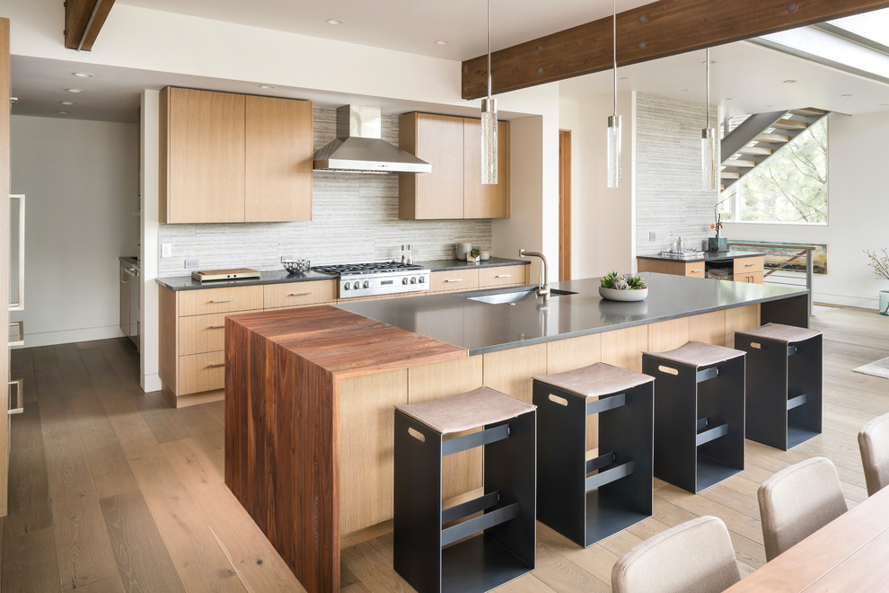 Contemporary l-shaped eat-in kitchen in Other with an undermount sink, shaker cabinets, light wood cabinets, grey splashback, panelled appliances, light hardwood floors, with island, brown floor and grey benchtop.