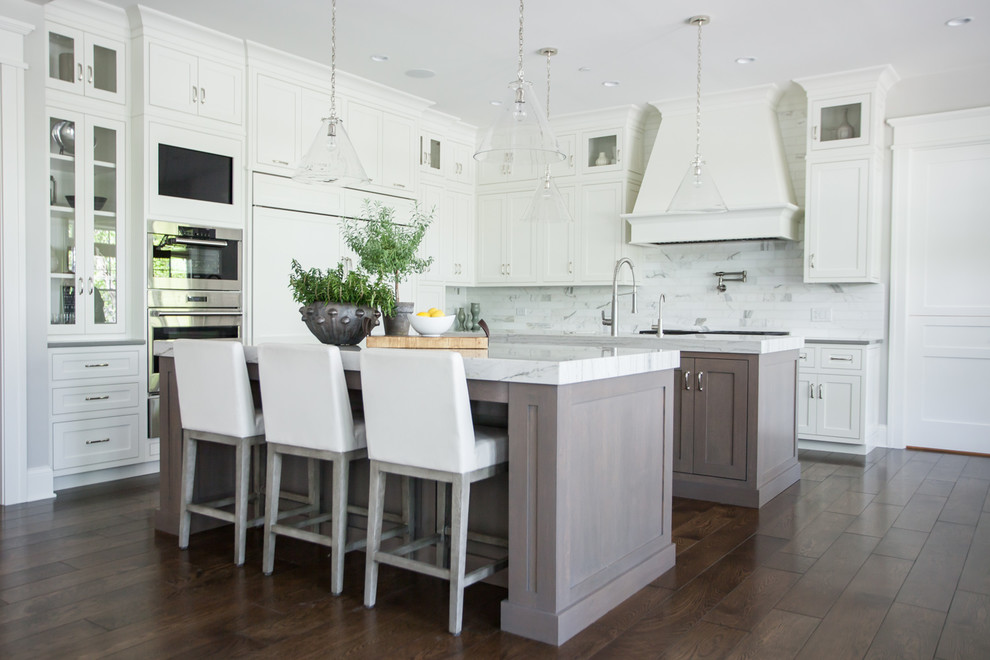 Design ideas for a transitional l-shaped eat-in kitchen in Chicago with shaker cabinets, medium wood cabinets, white splashback, stainless steel appliances, dark hardwood floors, multiple islands, brown floor and white benchtop.