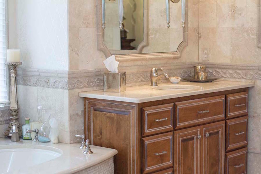 Design ideas for a mid-sized traditional master bathroom in Raleigh with raised-panel cabinets, medium wood cabinets, an alcove tub, a two-piece toilet, beige tile, limestone, beige walls, limestone floors, an undermount sink, limestone benchtops and beige floor.