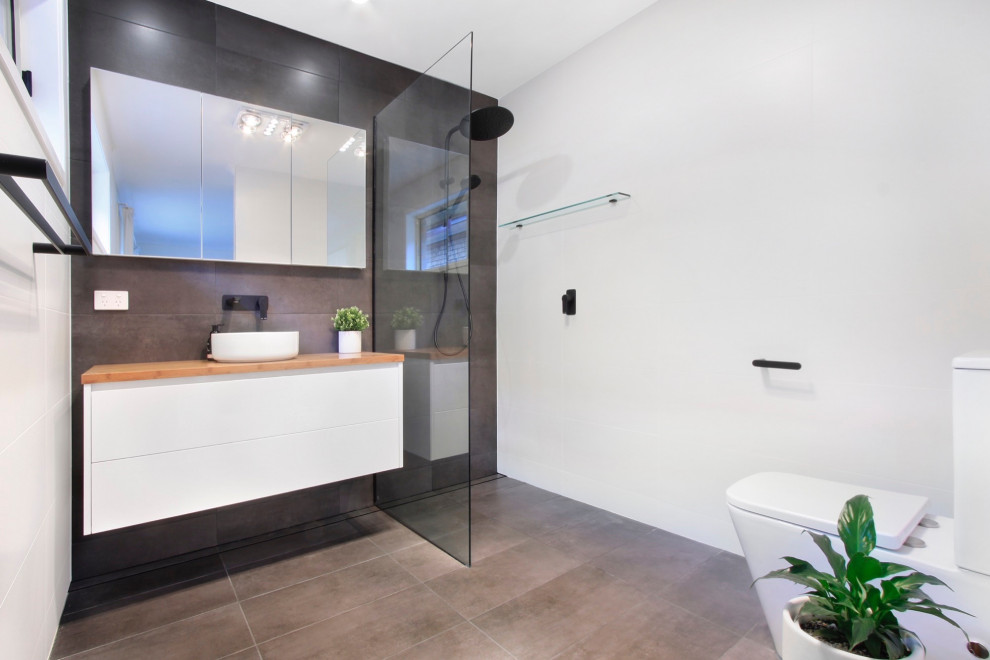 Photo of a mid-sized modern master wet room bathroom in Other with recessed-panel cabinets, white cabinets, a one-piece toilet, gray tile, ceramic tile, white walls, ceramic floors, a vessel sink, wood benchtops, multi-coloured floor, an open shower, brown benchtops, a single vanity and a floating vanity.