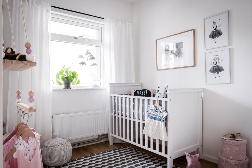 This is an example of a mid-sized scandinavian nursery for girls in Gothenburg with white walls, medium hardwood floors and brown floor.