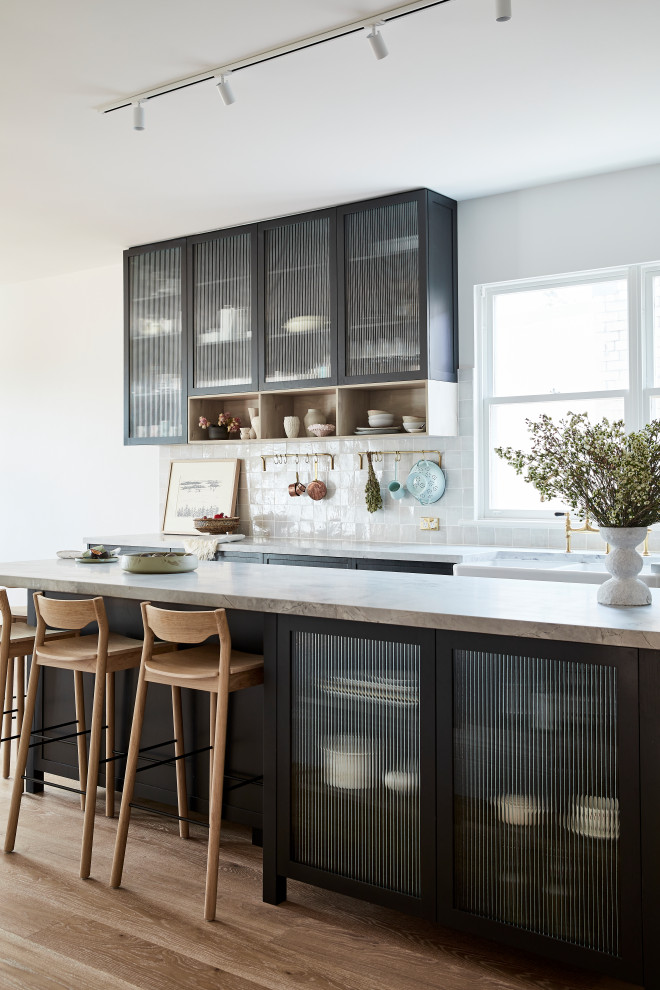 Inspiration for a mid-sized transitional l-shaped eat-in kitchen in Sydney with a farmhouse sink, shaker cabinets, black cabinets, marble benchtops, grey splashback, ceramic splashback, stainless steel appliances, light hardwood floors, with island, brown floor and grey benchtop.