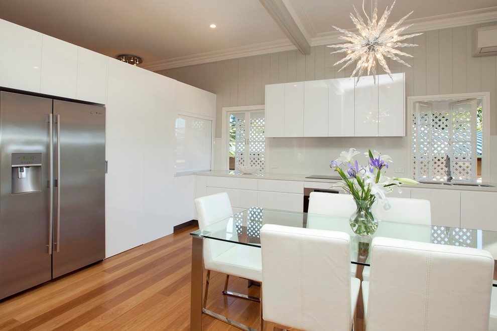 Design ideas for an expansive contemporary l-shaped eat-in kitchen in Brisbane with a double-bowl sink, flat-panel cabinets, white cabinets, solid surface benchtops, white splashback, glass sheet splashback, stainless steel appliances, light hardwood floors and no island.