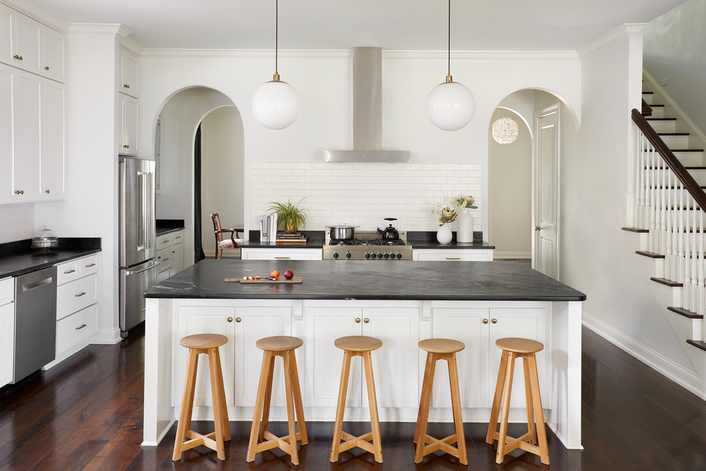 Design ideas for a transitional kitchen in Nashville with shaker cabinets, white cabinets, white splashback, subway tile splashback, stainless steel appliances, dark hardwood floors, with island and brown floor.