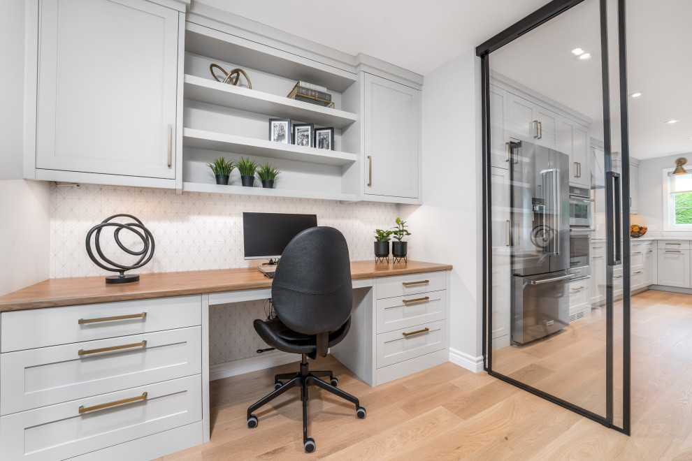 Diseño de despacho actual de tamaño medio con paredes grises, suelo de madera clara, escritorio empotrado, suelo marrón y papel pintado