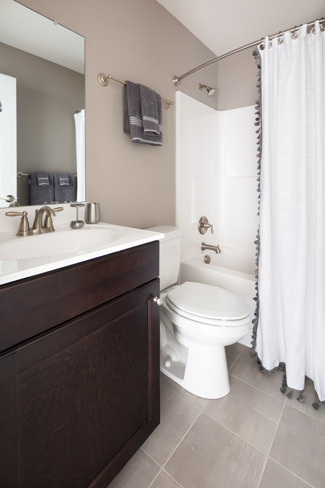 Design ideas for a mid-sized transitional master bathroom in Other with recessed-panel cabinets, brown cabinets, an alcove tub, a shower/bathtub combo, a two-piece toilet, beige tile, beige walls, ceramic floors, an integrated sink, solid surface benchtops, grey floor, a shower curtain and white benchtops.