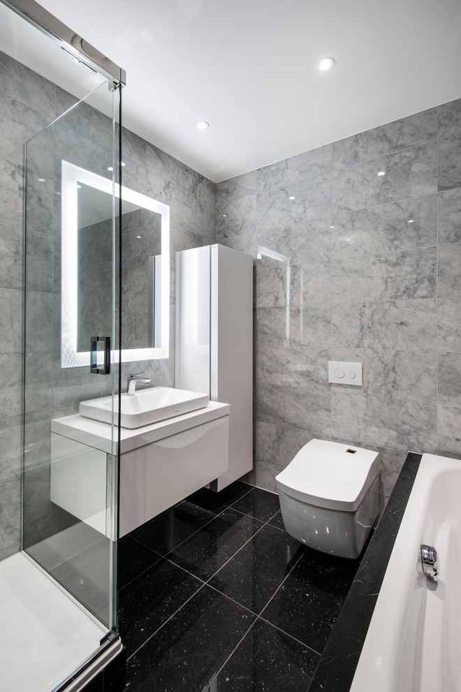 Photo of a mid-sized contemporary bathroom in London with beaded inset cabinets, brown cabinets, a wall-mount toilet, gray tile, stone tile, grey walls, marble floors, a vessel sink and marble benchtops.