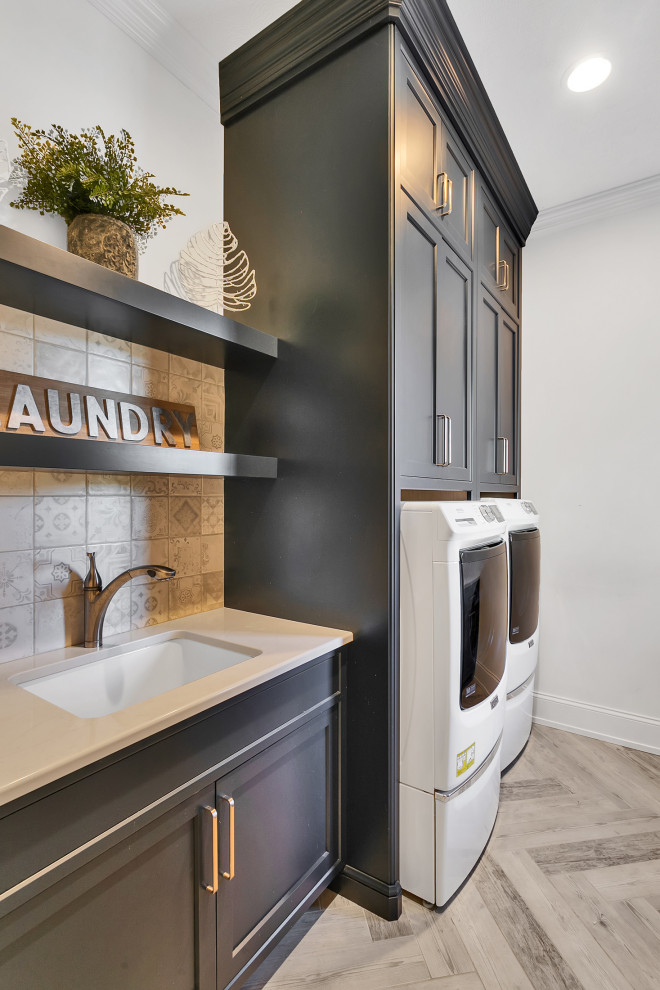 Inspiration for an expansive modern galley dedicated laundry room in Other with an undermount sink, beaded inset cabinets, black cabinets, quartzite benchtops, grey splashback, mosaic tile splashback, grey walls, porcelain floors, an integrated washer and dryer, grey floor, beige benchtop and vaulted.