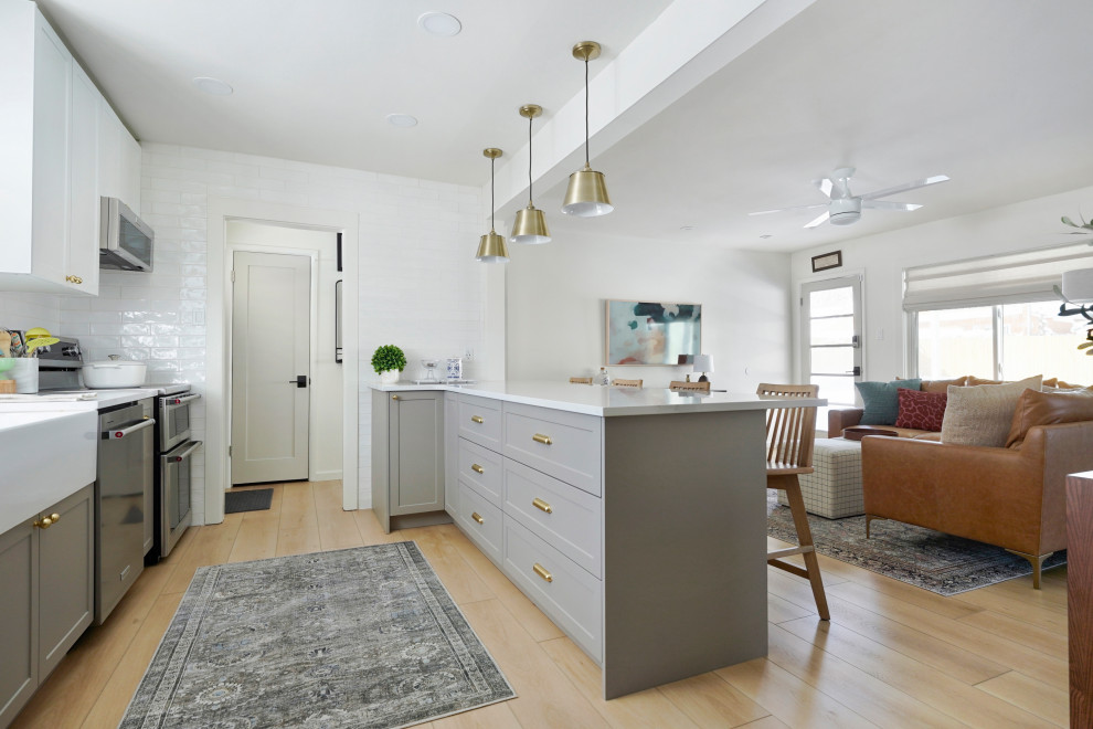 Design ideas for a mid-sized modern kitchen in Denver with a farmhouse sink, shaker cabinets, grey cabinets, granite benchtops, white splashback, ceramic splashback, stainless steel appliances, vinyl floors, with island and white benchtop.