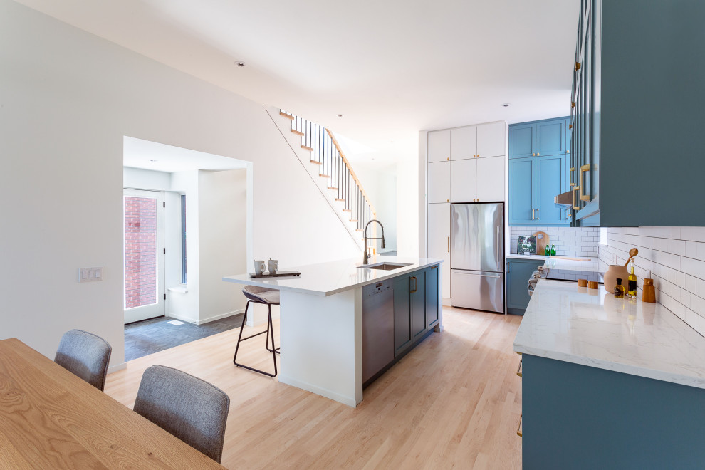 Photo of a mid-sized modern galley eat-in kitchen in Ottawa with an undermount sink, quartz benchtops, white splashback, subway tile splashback, stainless steel appliances, light hardwood floors, with island, brown floor and white benchtop.