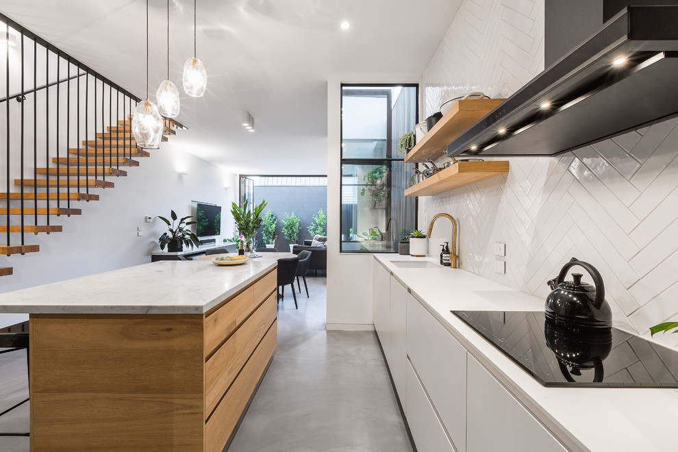 Design ideas for a mid-sized contemporary l-shaped eat-in kitchen in Melbourne with an undermount sink, flat-panel cabinets, medium wood cabinets, marble benchtops, white splashback, concrete floors, with island, grey floor, mosaic tile splashback and black appliances.