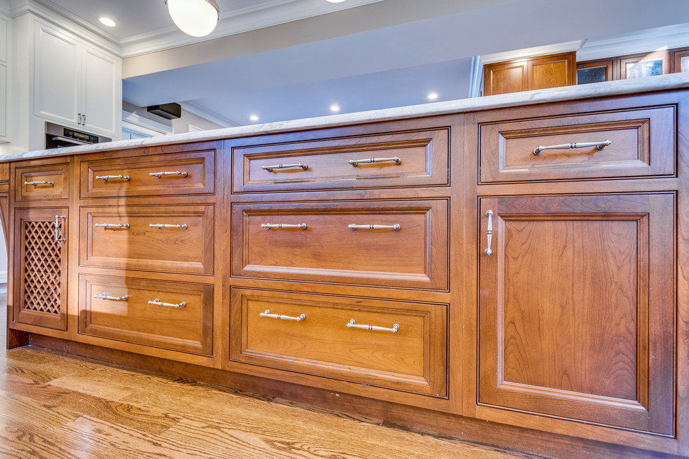 Mid-sized transitional l-shaped medium tone wood floor and brown floor open concept kitchen photo in Boston with a farmhouse sink, recessed-panel cabinets, white cabinets, onyx countertops, beige backsplash, ceramic backsplash, stainless steel appliances and an island