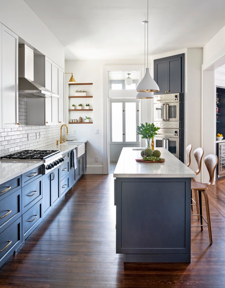 Inspiration for a transitional kitchen in San Francisco with a farmhouse sink, white cabinets, quartz benchtops, white splashback, stainless steel appliances, medium hardwood floors, with island, brown floor and white benchtop.
