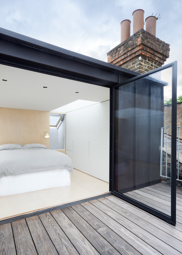 Photo of a contemporary master bedroom in London with white walls and plywood floors.
