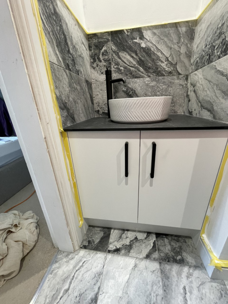 This is an example of a medium sized modern grey and white ensuite bathroom in Other with flat-panel cabinets, white cabinets, an alcove shower, a two-piece toilet, multi-coloured tiles, porcelain tiles, white walls, porcelain flooring, a vessel sink, laminate worktops, multi-coloured floors, a sliding door, black worktops, a single sink and a built in vanity unit.