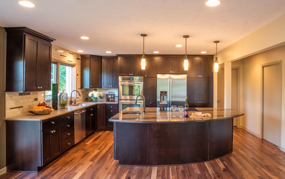Inspiration for a large transitional l-shaped eat-in kitchen remodel with an undermount sink, recessed-panel cabinets, dark wood cabinets, granite countertops, beige backsplash, stainless steel appliances, beige walls, engineered wood floors and an island