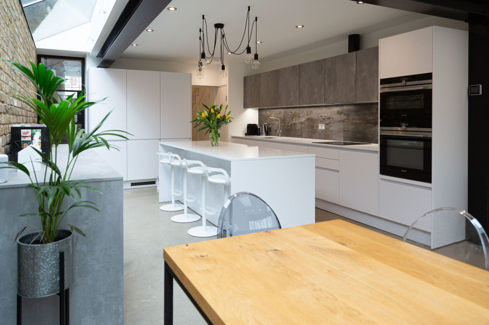 Design ideas for a large contemporary l-shaped eat-in kitchen in London with an undermount sink, flat-panel cabinets, white cabinets, solid surface benchtops, grey splashback, porcelain splashback, concrete floors, with island, grey floor, white benchtop and panelled appliances.