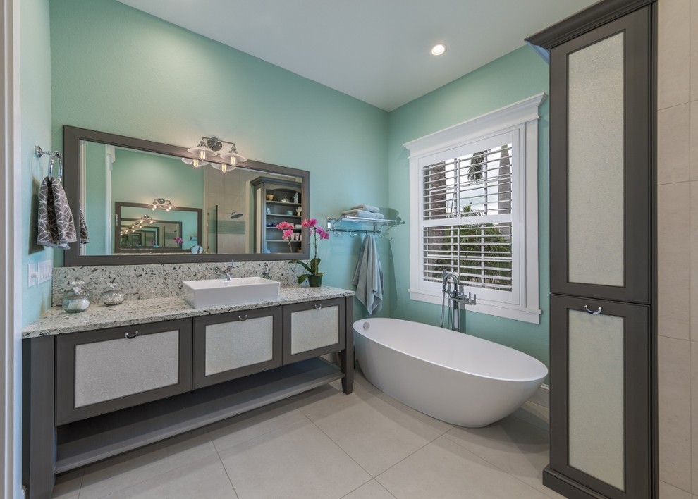 Mid-sized beach style 3/4 bathroom in Tampa with a vessel sink, grey cabinets, a freestanding tub, blue walls, an open shower, a one-piece toilet, black tile, gray tile, white tile, stone slab, ceramic floors, granite benchtops and shaker cabinets.